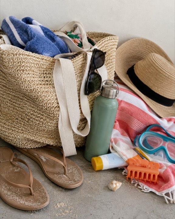A straw tote, flip-flops, sunglasses, a sun hat, and beach towels