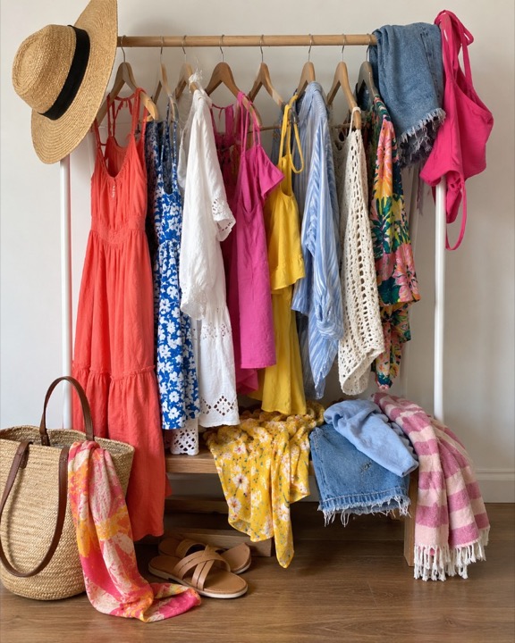 A rack of summer dresses, shorts, and a straw hat